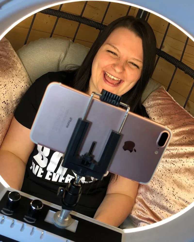 Amy Woodward laughing on camera, filming on her phone under a ring light